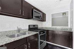 kitchen featuring light stone counters, sink, stainless steel appliances, and dark brown cabinets