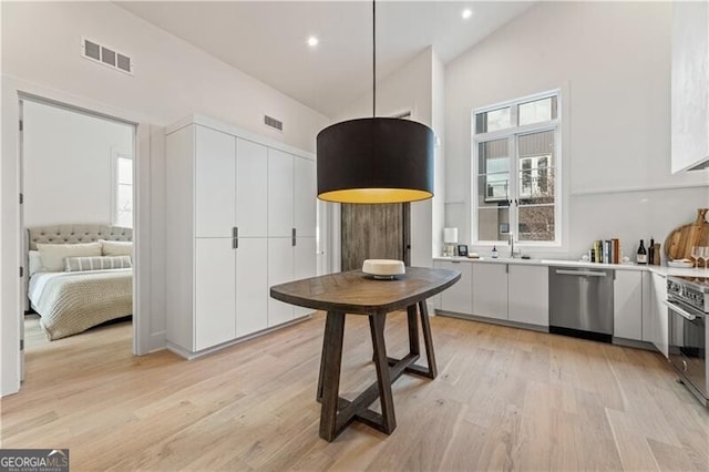 kitchen with sink, stainless steel appliances, decorative light fixtures, white cabinets, and light wood-type flooring