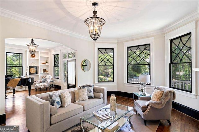 living room with built in shelves, wood-type flooring, ornamental molding, and a chandelier