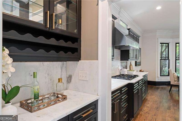 kitchen featuring stainless steel gas stovetop, wall chimney range hood, crown molding, tasteful backsplash, and wood-type flooring