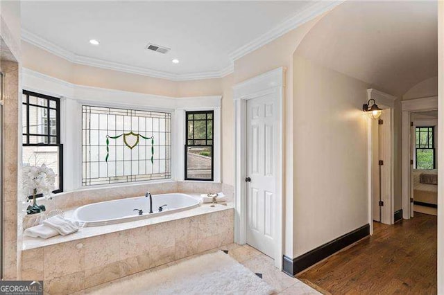 bathroom featuring wood-type flooring, crown molding, and tiled tub