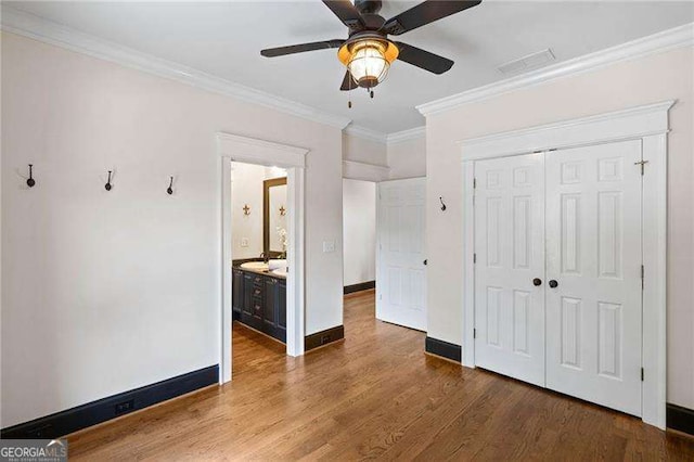 unfurnished bedroom with connected bathroom, ceiling fan, crown molding, wood-type flooring, and a closet