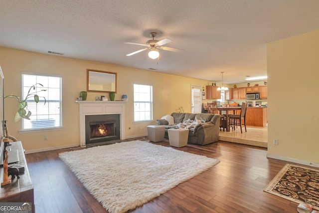 living room with a textured ceiling, ceiling fan, and dark hardwood / wood-style floors