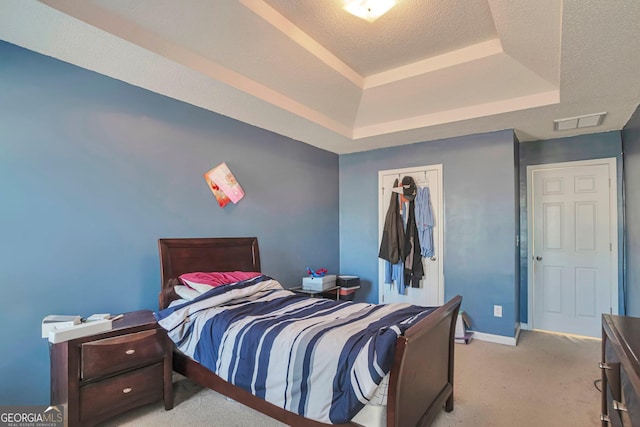 bedroom featuring a textured ceiling, a tray ceiling, a closet, and light colored carpet