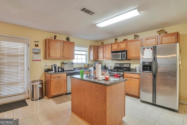 kitchen with a textured ceiling, a center island, stainless steel appliances, and light tile patterned floors