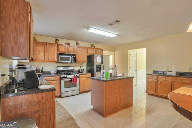 kitchen with a textured ceiling, a kitchen island, light tile patterned flooring, and stainless steel appliances