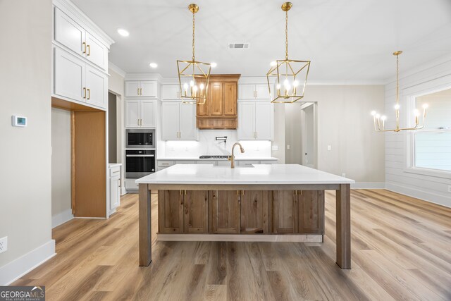 kitchen with light stone countertops, sink, decorative light fixtures, a kitchen island with sink, and white cabinets