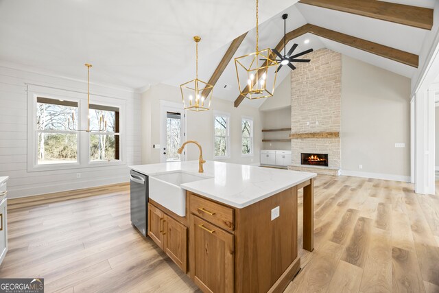 kitchen with pendant lighting, sink, vaulted ceiling with beams, a fireplace, and an island with sink