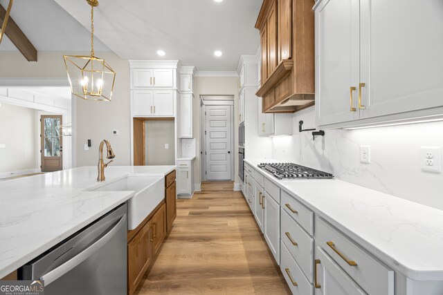 kitchen with light stone counters, a kitchen island with sink, sink, white cabinetry, and hanging light fixtures