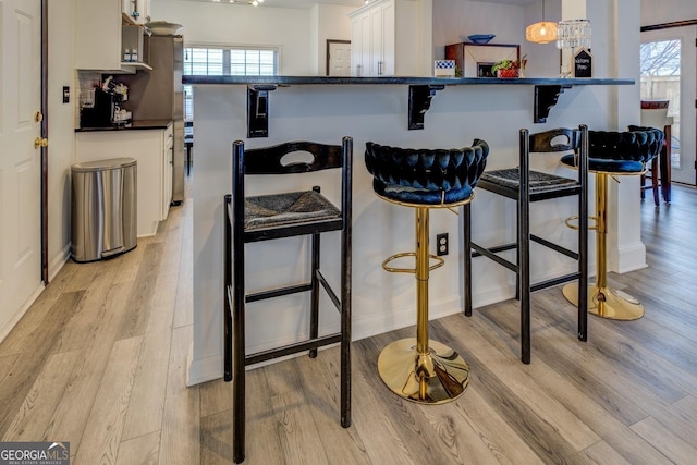 kitchen with a kitchen breakfast bar, decorative light fixtures, light hardwood / wood-style floors, and white cabinets