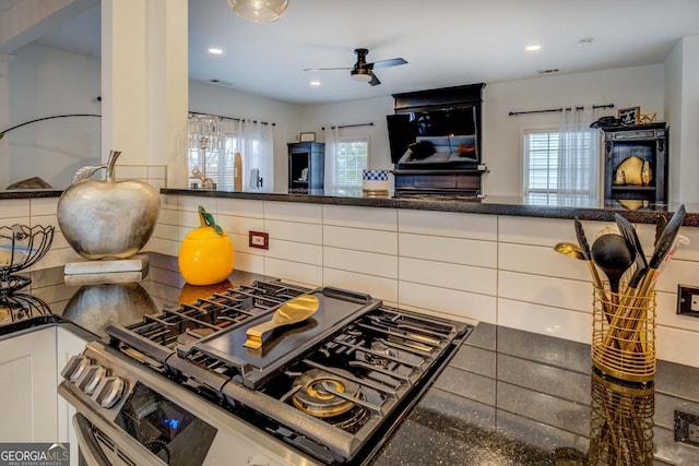 kitchen with tasteful backsplash, white cabinetry, gas range, and ceiling fan