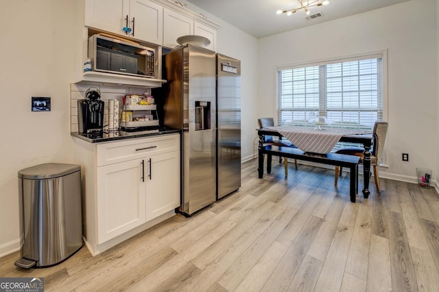 kitchen with built in microwave, white cabinetry, stainless steel fridge, dark stone counters, and light hardwood / wood-style flooring