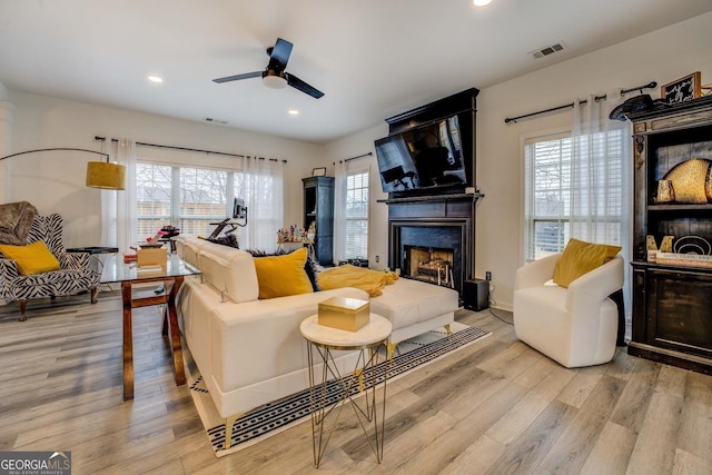 living room featuring ceiling fan, a fireplace, and light hardwood / wood-style flooring