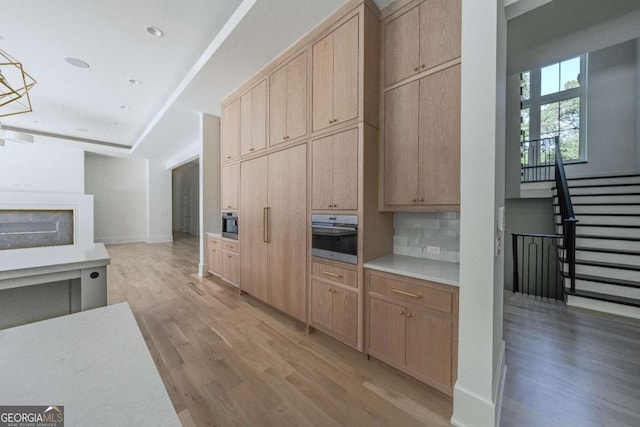 kitchen featuring pendant lighting, oven, light wood-type flooring, light brown cabinetry, and tasteful backsplash