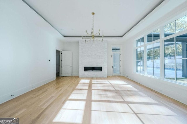 unfurnished living room featuring a raised ceiling, a stone fireplace, light hardwood / wood-style floors, and a notable chandelier