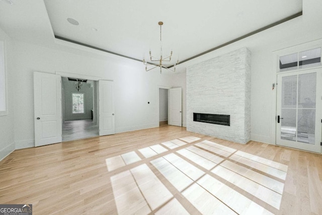 unfurnished living room featuring a tray ceiling, a stone fireplace, light wood-type flooring, and a notable chandelier