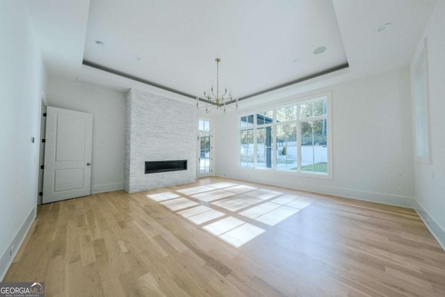 unfurnished living room featuring light hardwood / wood-style flooring, an inviting chandelier, a fireplace, and a tray ceiling