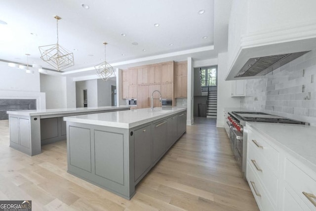 kitchen with gray cabinetry, a center island with sink, white cabinets, sink, and decorative light fixtures