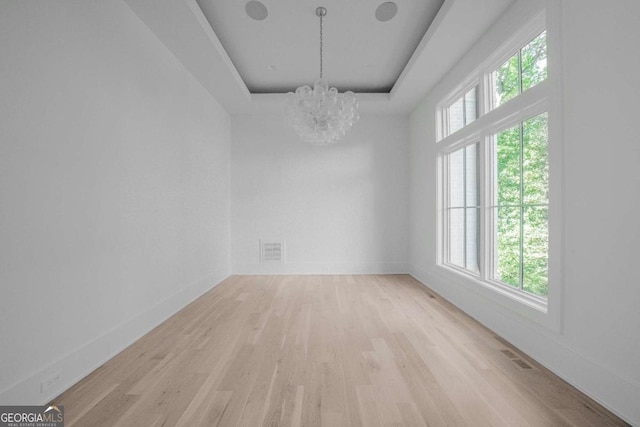 unfurnished room with a tray ceiling, an inviting chandelier, a wealth of natural light, and light hardwood / wood-style flooring