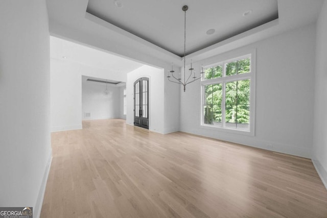 unfurnished dining area with a raised ceiling, light hardwood / wood-style floors, and an inviting chandelier