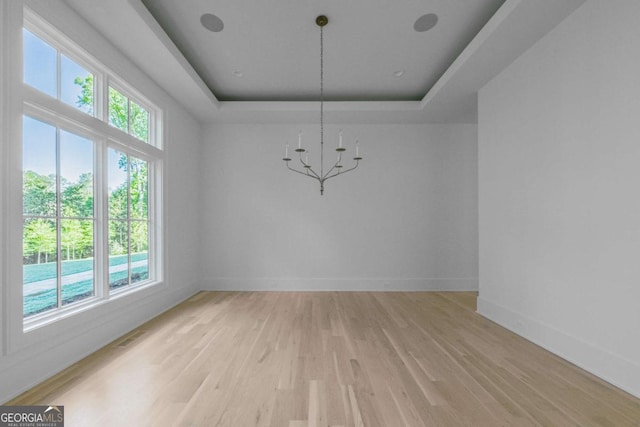 unfurnished dining area with a tray ceiling, light hardwood / wood-style flooring, and a chandelier