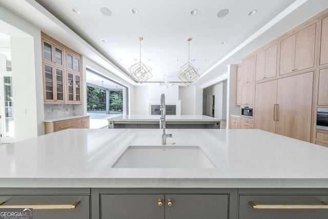 kitchen featuring light brown cabinets, sink, an island with sink, tasteful backsplash, and decorative light fixtures