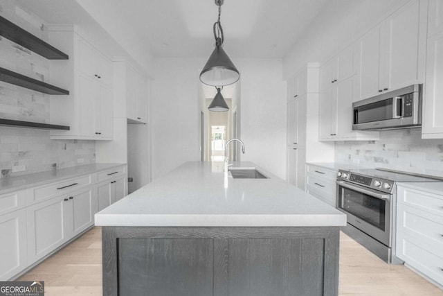 kitchen with white cabinets, hanging light fixtures, sink, an island with sink, and appliances with stainless steel finishes