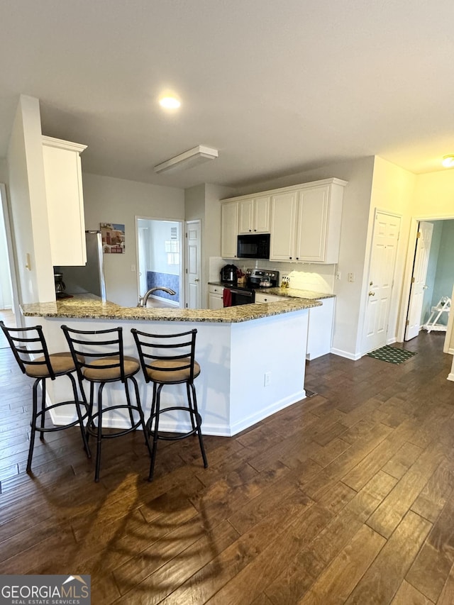 kitchen with kitchen peninsula, a breakfast bar, stainless steel appliances, dark wood-type flooring, and white cabinets