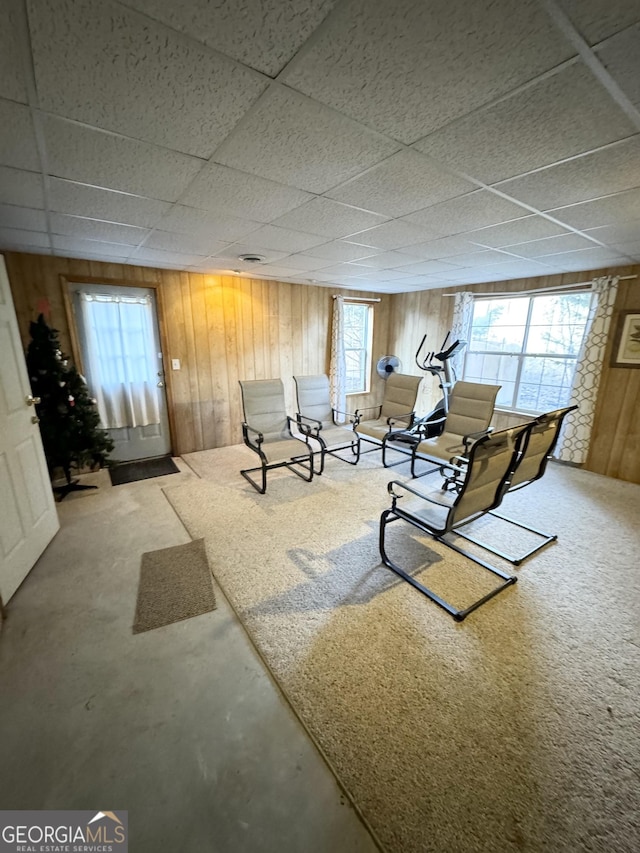 interior space featuring wooden walls, a drop ceiling, concrete flooring, and a wealth of natural light