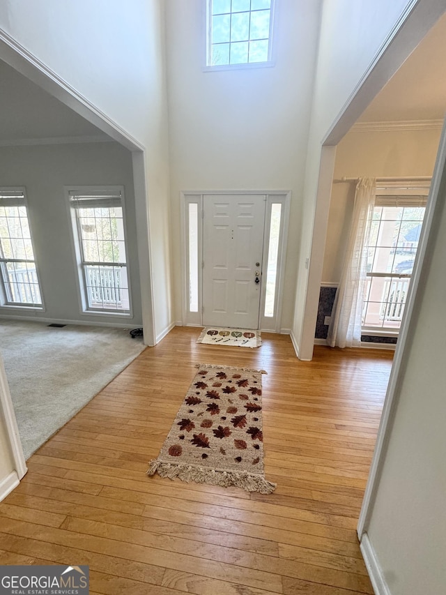 entrance foyer with a high ceiling, light wood-type flooring, and ornamental molding