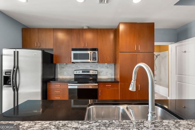 kitchen featuring appliances with stainless steel finishes, backsplash, dark stone countertops, and sink