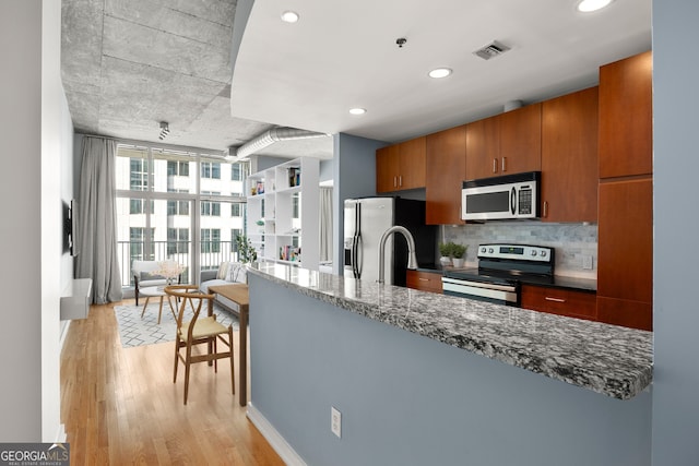 kitchen with decorative backsplash, light wood-type flooring, expansive windows, dark stone counters, and stainless steel appliances