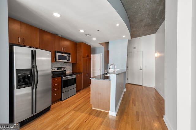 kitchen featuring appliances with stainless steel finishes, light wood-type flooring, tasteful backsplash, sink, and dark stone countertops