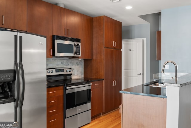 kitchen featuring backsplash, stainless steel appliances, sink, dark stone countertops, and light hardwood / wood-style floors