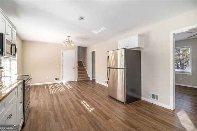 kitchen with light stone countertops, dark wood-type flooring, a notable chandelier, white cabinets, and appliances with stainless steel finishes