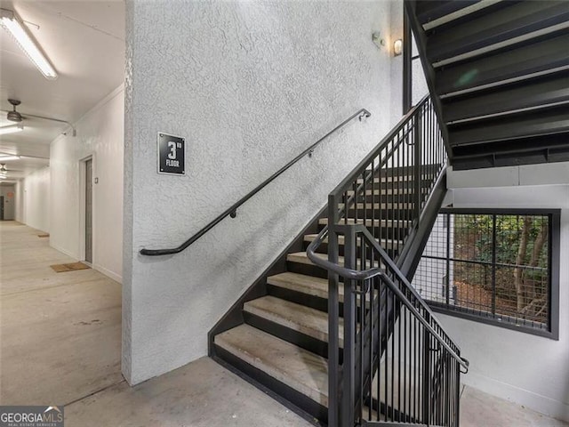 staircase featuring ceiling fan and concrete floors