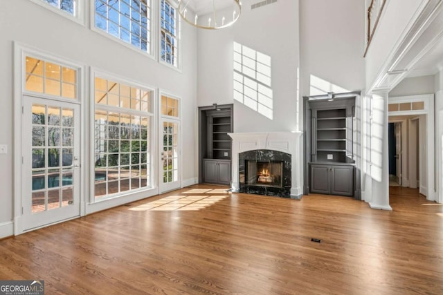 unfurnished living room featuring wood-type flooring, a towering ceiling, and a premium fireplace