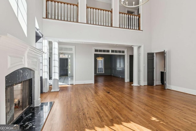 living room featuring decorative columns, a premium fireplace, hardwood / wood-style floors, and a towering ceiling