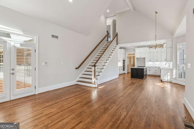 unfurnished living room with sink, high vaulted ceiling, a chandelier, beamed ceiling, and dark hardwood / wood-style floors