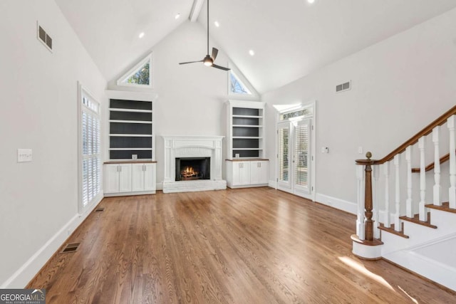 unfurnished living room featuring hardwood / wood-style floors, high vaulted ceiling, a brick fireplace, ceiling fan, and beamed ceiling