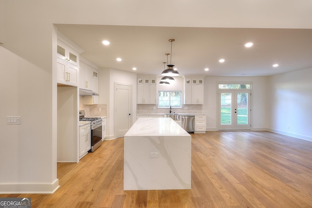 kitchen with stainless steel appliances, a kitchen island, light stone counters, decorative backsplash, and white cabinets