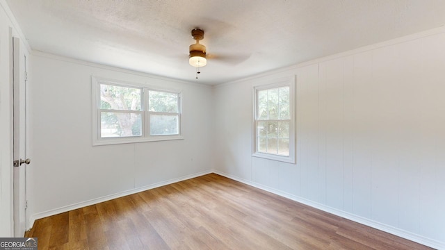 empty room with a wealth of natural light, ceiling fan, ornamental molding, and light wood-type flooring