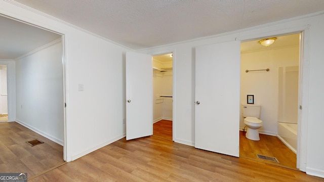 unfurnished bedroom with ensuite bath, a spacious closet, crown molding, light hardwood / wood-style floors, and a closet