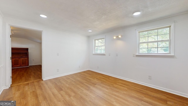 unfurnished room with a textured ceiling, lofted ceiling, and light wood-type flooring