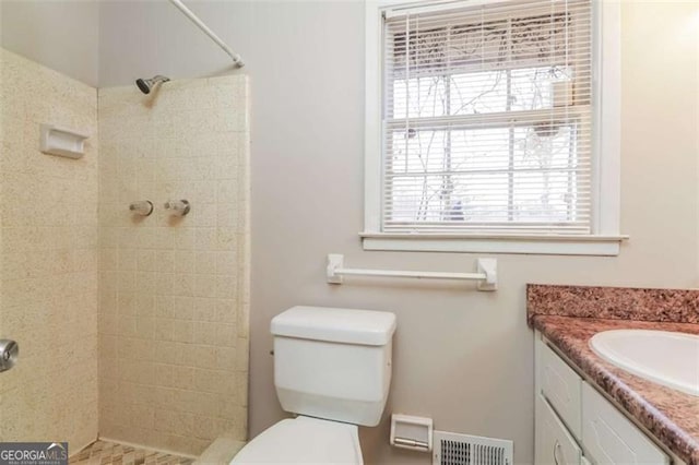 bathroom featuring toilet, a tile shower, plenty of natural light, and vanity