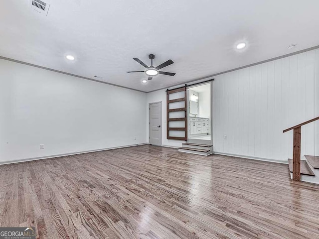 unfurnished living room with a barn door, ceiling fan, hardwood / wood-style floors, and ornamental molding