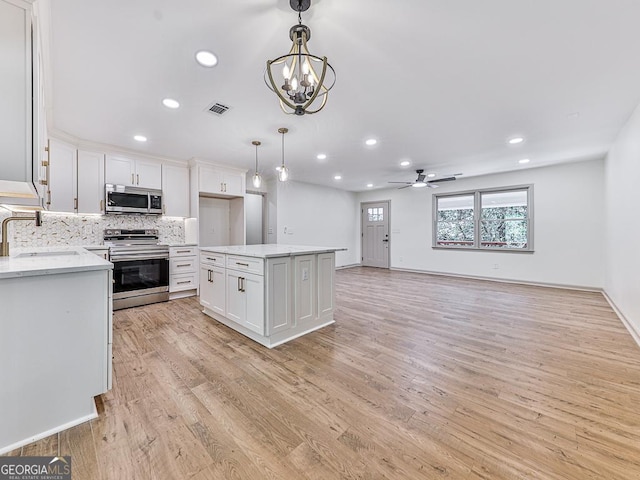 kitchen featuring decorative light fixtures, stainless steel appliances, a kitchen island, and white cabinetry