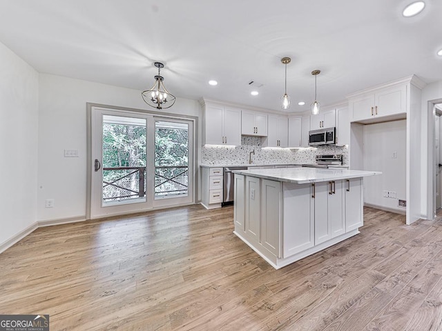 kitchen with a center island, white cabinets, hanging light fixtures, light wood-type flooring, and appliances with stainless steel finishes