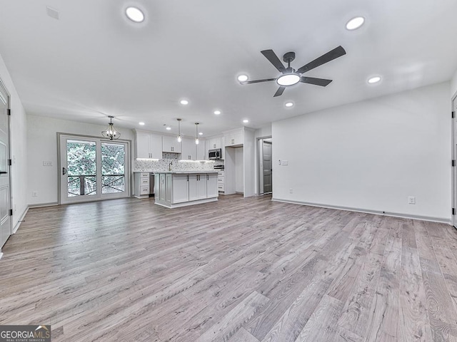 unfurnished living room with ceiling fan with notable chandelier and light hardwood / wood-style flooring