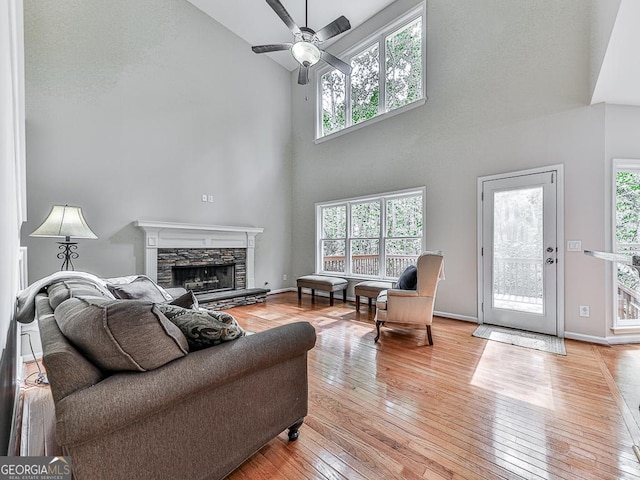 living room featuring ceiling fan, a fireplace, a high ceiling, and light hardwood / wood-style flooring